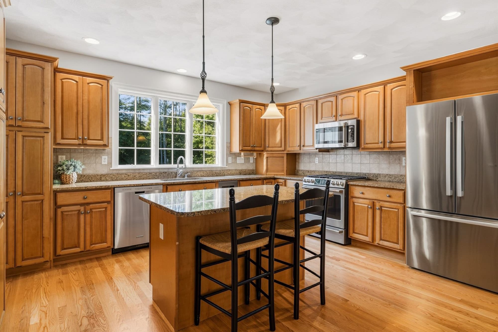 The kitchen with the granite island, gas range, stainless refrigerator, and a window over the sink