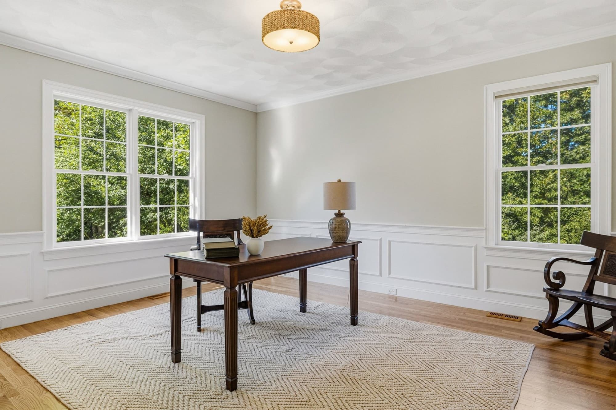 The office with a desk, wainscoting, and 2 windows over the front lawn