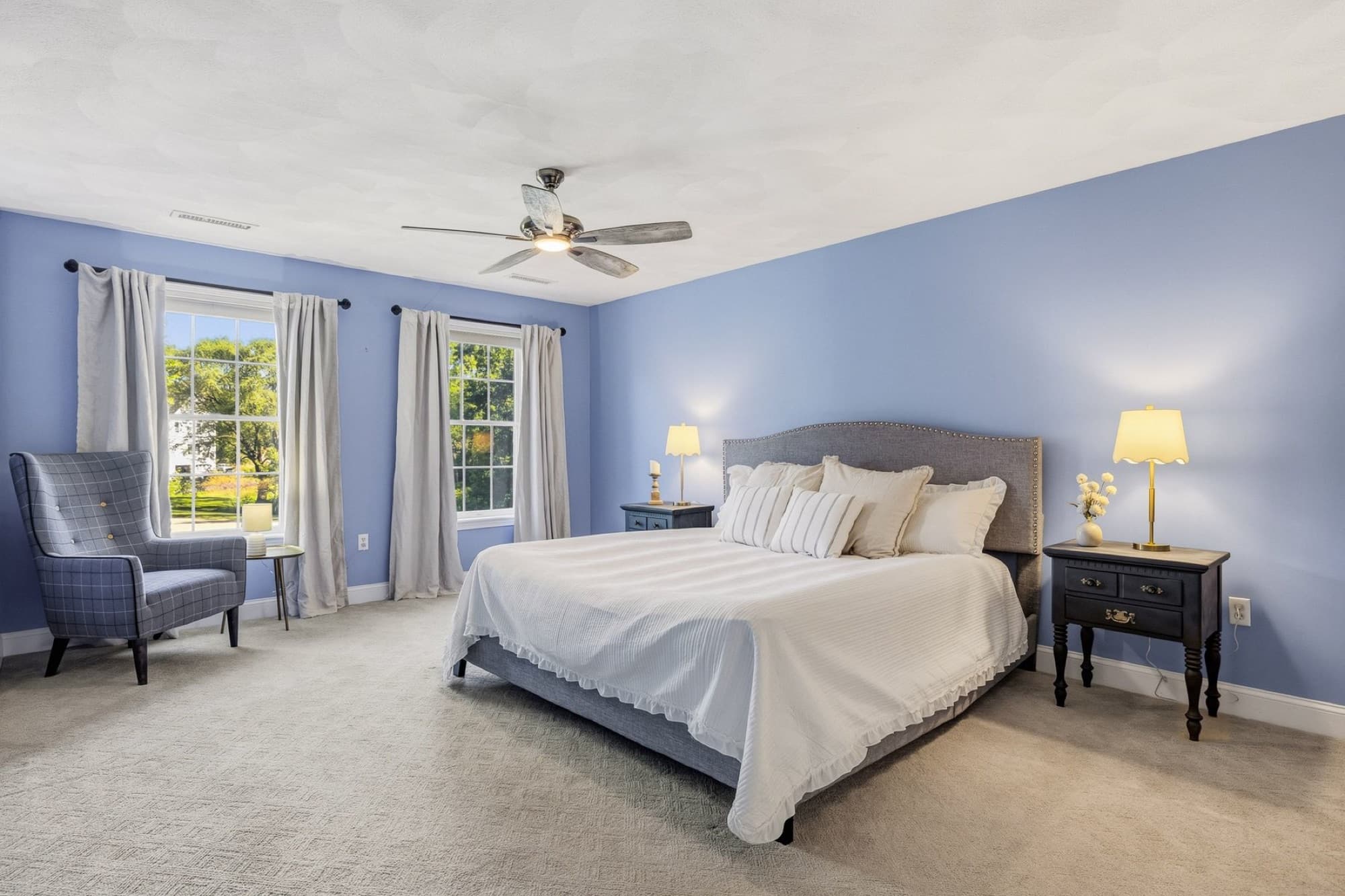 The primary bedroom with a ceiling fan, 2 windows, and a sitting chair