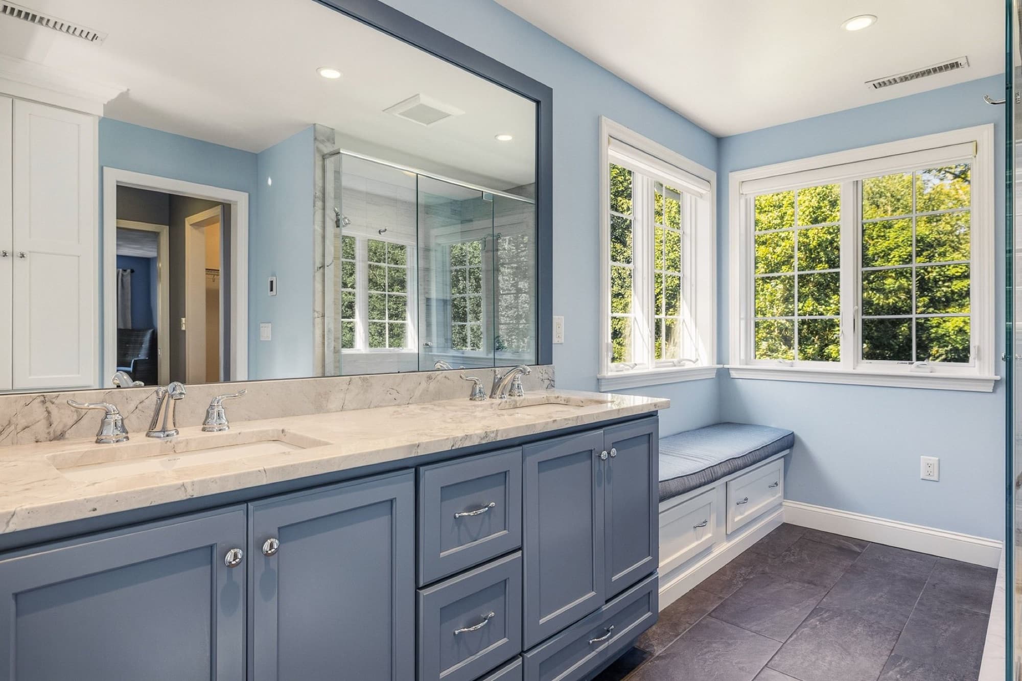 The primary bath with a double vanity, a window seat, and a wide mirror