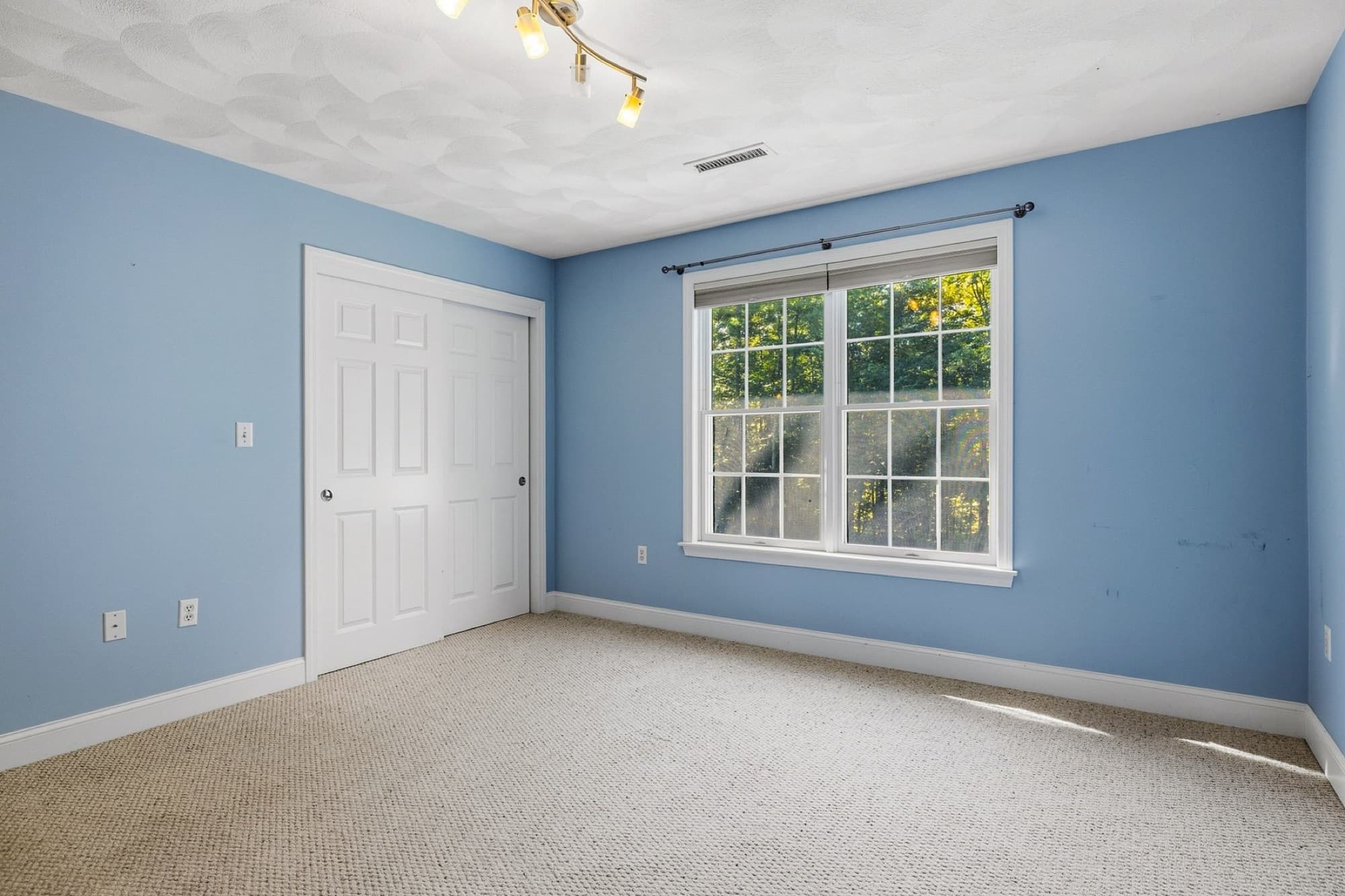 A blue bedroom with a double closet and a window